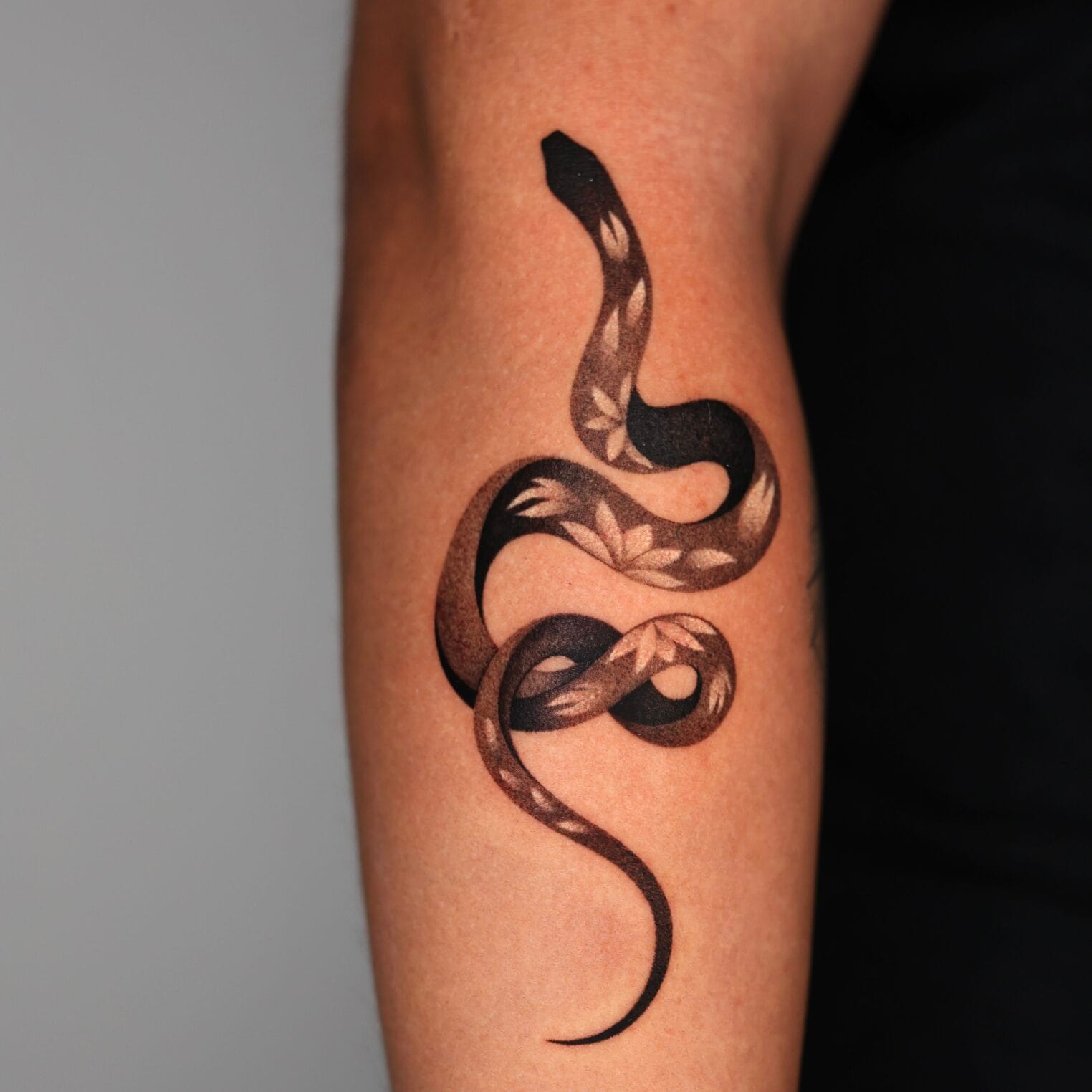 Black and Gray Snake Tattoo on Forearm with Floral Design